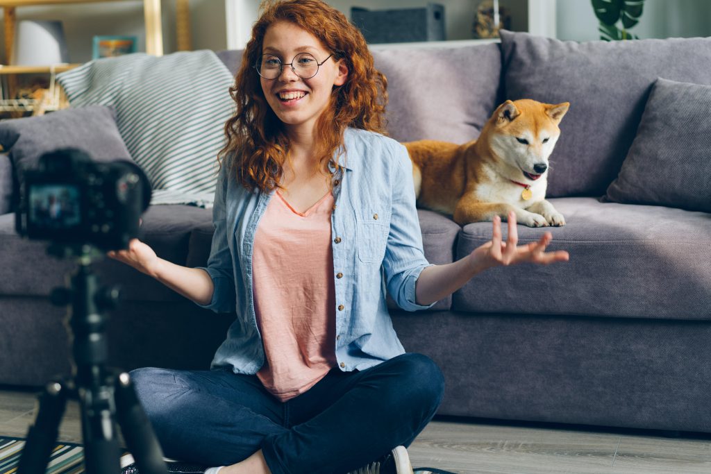 Lächelnde junge Vloggerin mit ihrem Hund erstellt authentischen Content für Social Media.