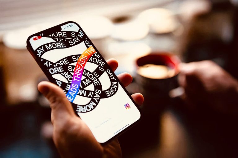 Hand holding smartphone with the new social media app "Threads" from Meta, a coffee cup in the background.